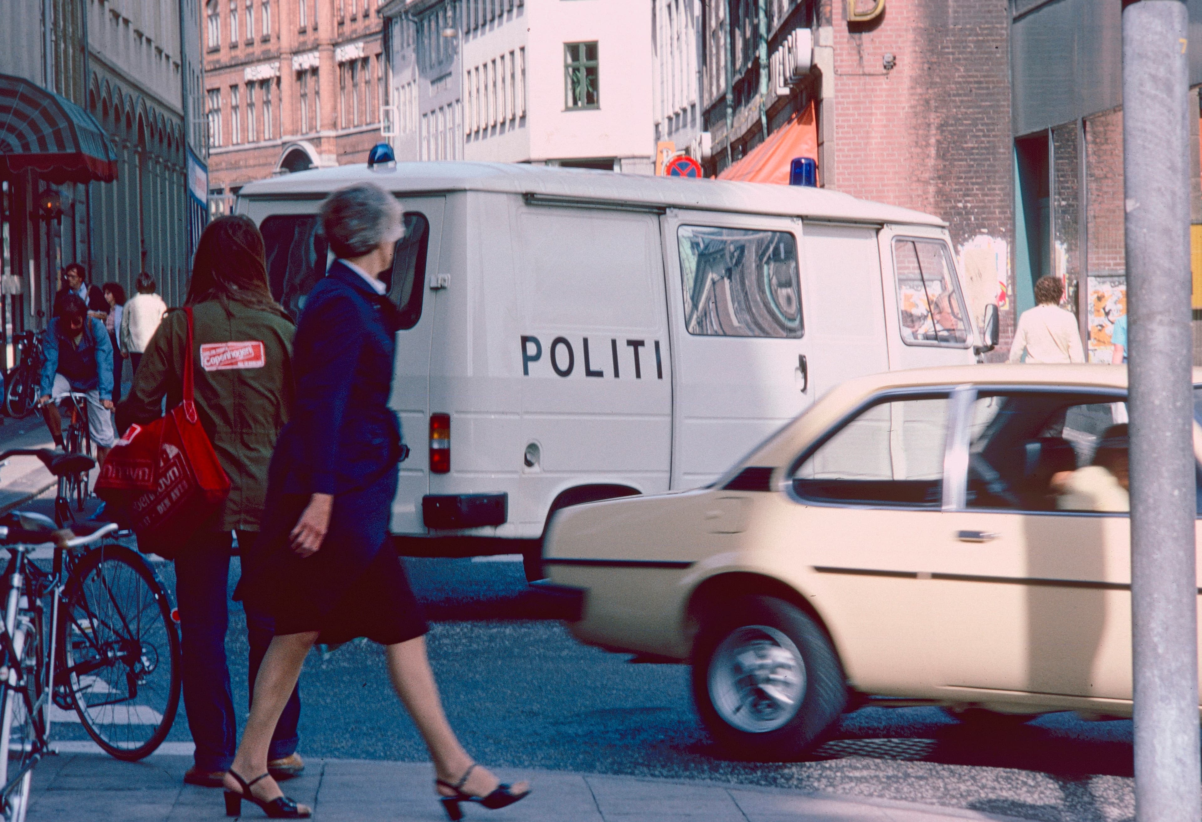 To fodgængere passerer en parkeret politibil på en byvej